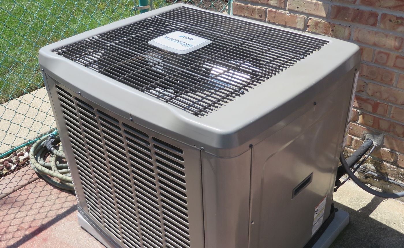 Central air conditioning condenser beside a brick house